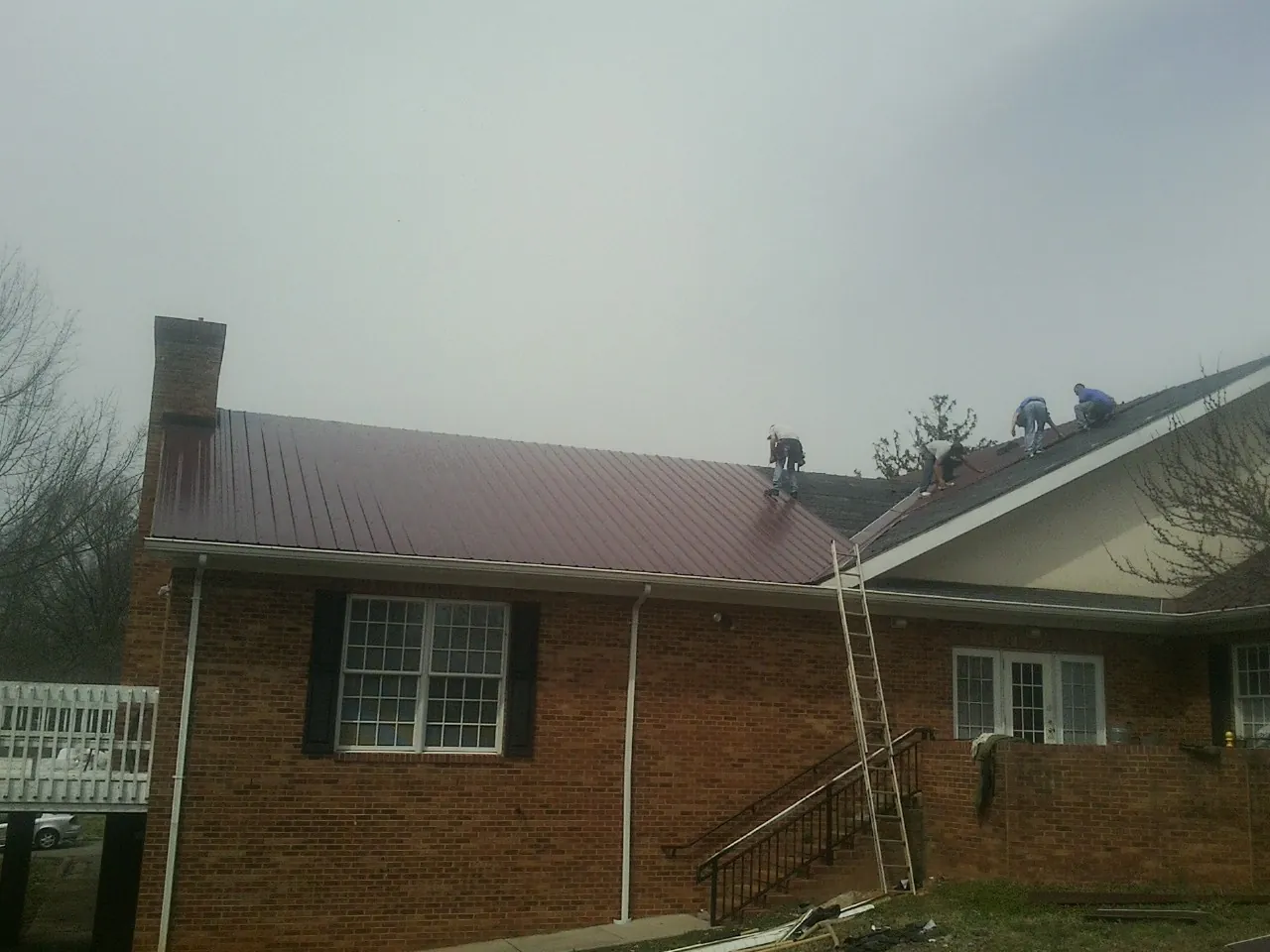 Crew setting red metal roofing panels on a brick home in Haines City