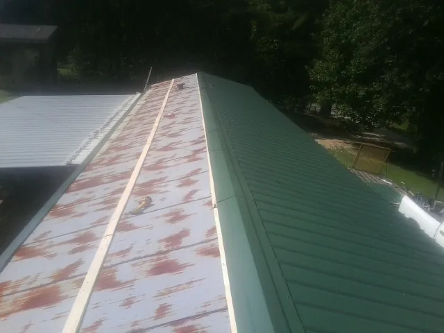 Old rusted panels beside newly installed green metal roofing — Wind Damage Roof Repair by Roofing Brothers in Haines City