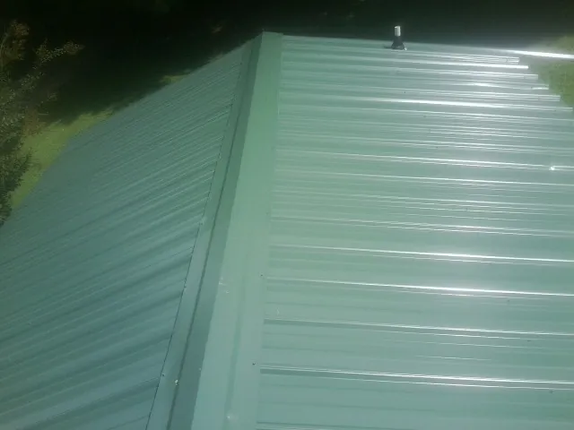 New green metal panels meeting at the ridge of a roof — Flat Roof Repair work by our crew in Haines City