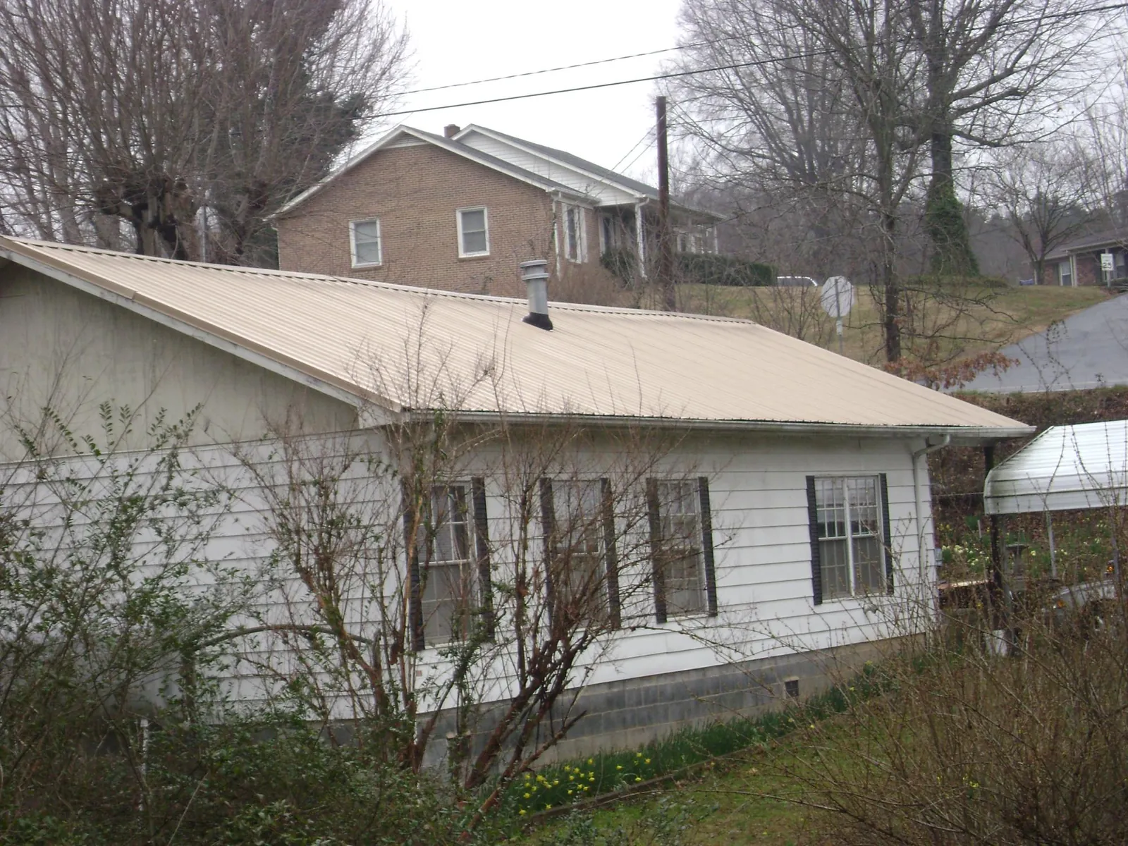 Tan metal roof on a white sided house set into a hillside — Commercial Roofing by Roofing Brothers in Haines City